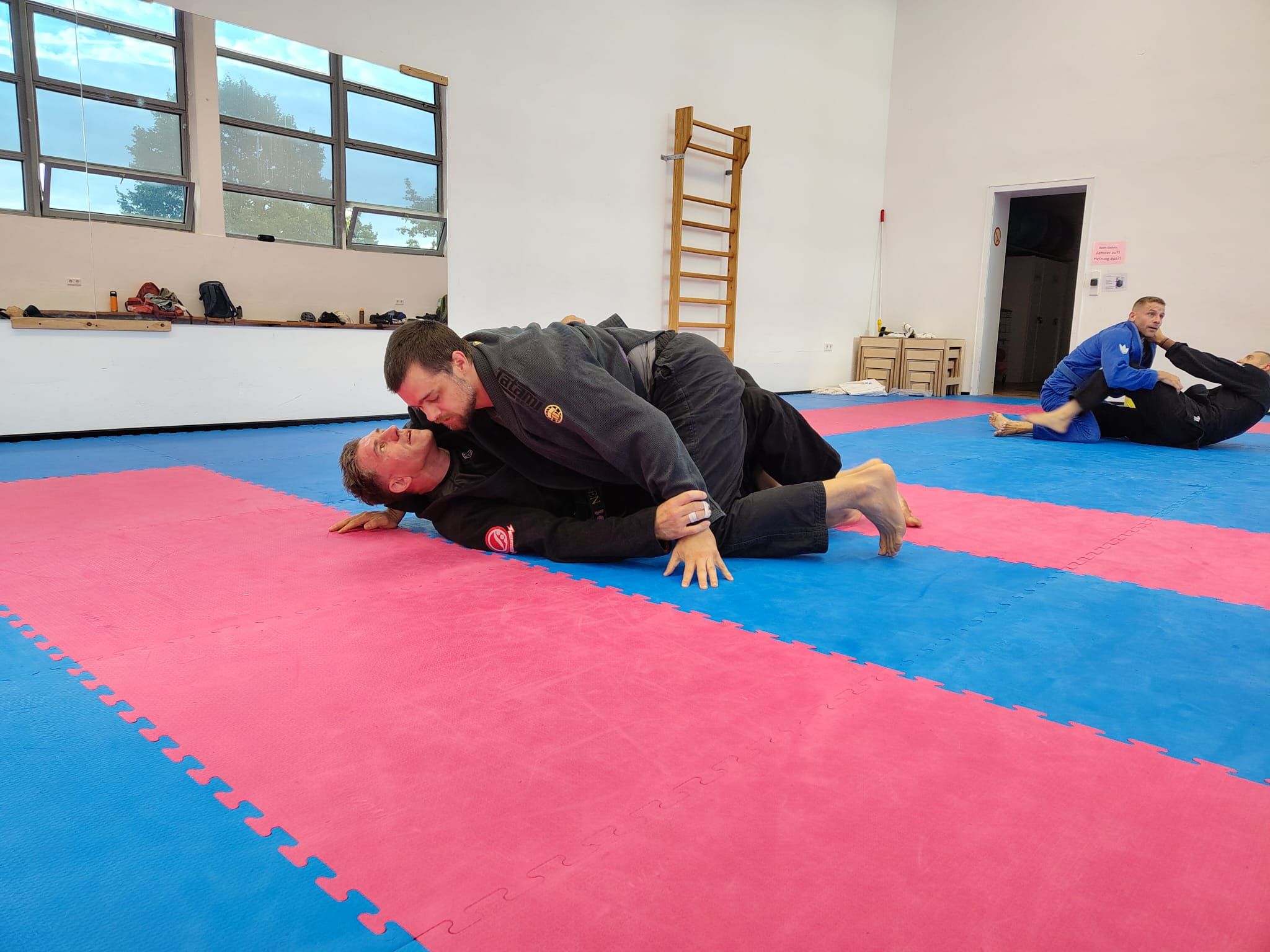 Zwei Trainingspartner im Gi üben eine Position am Boden im Athleticon