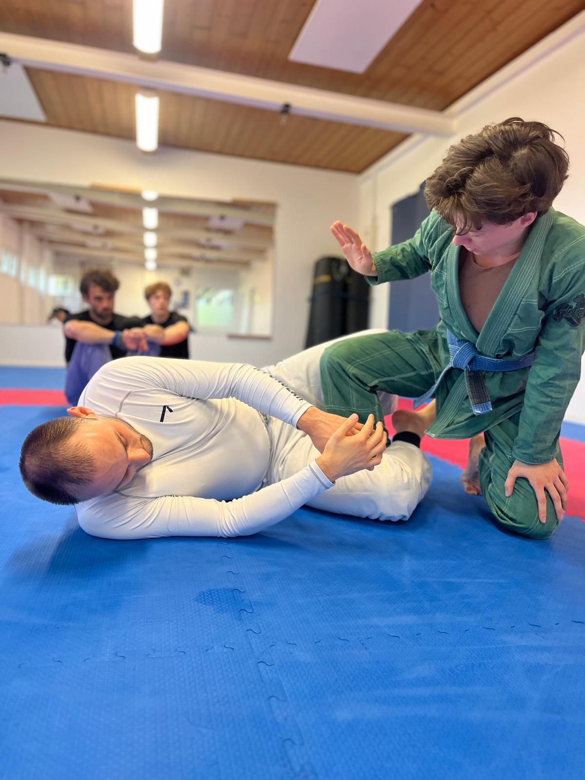 Zwei Trainingspartner üben eine Technik aus der Guard, im Hintergrund weitere Teilnehmer